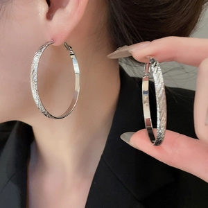 Detail of silver hoop earrings featuring a textured twill pattern on the metal surface