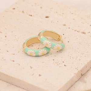 Détail de boucles d'oreilles marguerites vert menthe et dorées sur pierre beige