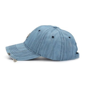 Detailed macro of denim baseball cap featuring metallic cross studs and safety pin accent