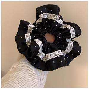 Detail of black polka dot scrunchie with white lace trim held against a white wall