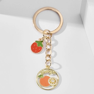 Detailed macro view of creative strawberry and orange enamel pendants on gold keychain