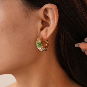 Détail d'une boucle d'oreille dorée vintage avec perles vertes et blanches sur mannequin