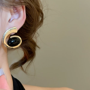 Close-up of geometric gold hammer-textured earring with an oval black gemstone inlay