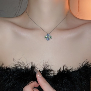 Detail of four-petal flower necklace with blue and green gems on female collarbone