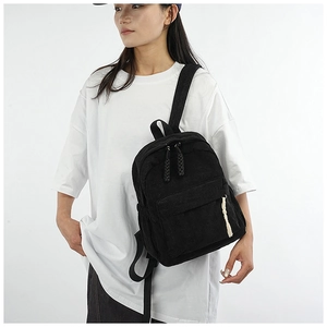 Detail of black corduroy backpack on model highlighting textured fabric and zipper pocket