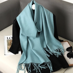 Close-up of a teal blue cashmere-feel scarf featuring soft tassels on a sofa setting