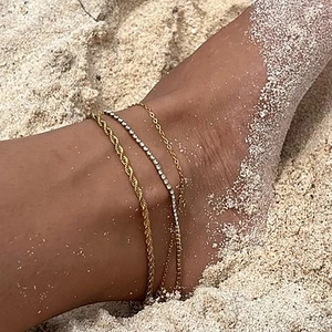 Three-piece gold twisted rope and rhinestone anklet set worn on a sunny beach