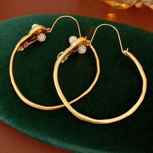 Close-up of matte gold hoop earrings with sparkling rhinestone ball detail on green velvet