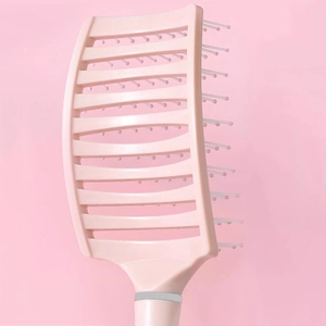 Brosse à cheveux incurvée rose pour massage du cuir chevelu et coiffage volumineux sur fond uni