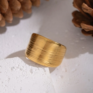 Minimalist wide gold-plated textured ring with horizontal brushed patterns on stone stand