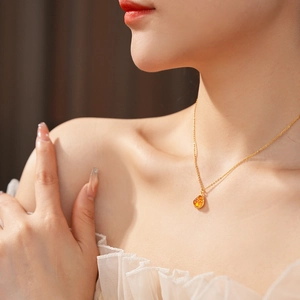 Detail of amber gourd pendant on gold chain necklace worn by a model in soft lighting