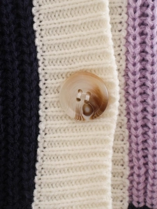 Dettaglio macro del cardigan in maglia color-block con bottone marmorizzato e coste