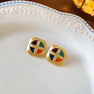 Macro detail of vintage gold square earrings with colorful enamel cross pattern on ceramic