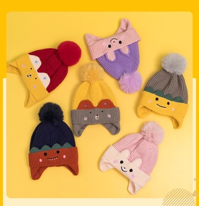 Flat lay view of colorful knitted kids' hats with ear flaps and large pom-poms in six colors