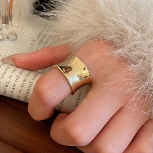 Close-up of a wide gold textured ring worn on a finger against a cozy lifestyle background