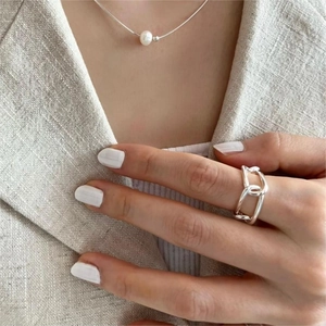 Detail of 925 silver chain link ring and pearl necklace on a model wearing a linen blazer