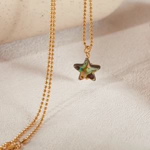 Macro shot of gold star pendant with iridescent abalone shell inlay on a bead chain