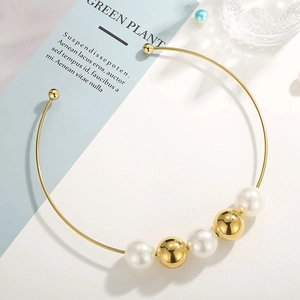 Detail of gold choker necklace featuring polished metal spheres and white pearl accents