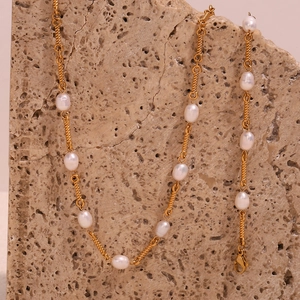 Detail of freshwater pearl necklace with gold spiral chain on a beige stone surface