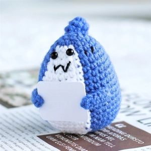 Detail of blue crochet shark plush holding an emotional support sign on a book