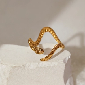Close-up of golden snake ring with detailed scale texture resting on a white rock