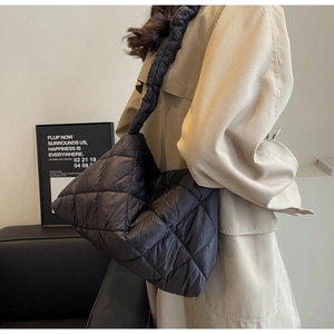 Detail of black quilted shoulder bag with glossy nylon finish shown on a model