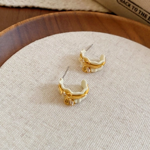 Detail of 18k gold plated C-shaped hoop earrings with white enamel bow and crystal charm