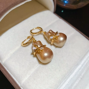 Vue macro de boucles d'oreilles nœud dorées à l'or 18k avec perles baroques et zircon