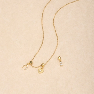 Detailed shot of golden necklace featuring horseshoe, heart charms and zircon details