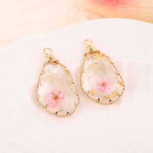 Pink dried flower resin pendant with gold wire trim in teardrop shape on white ceramic