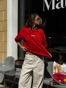 Scatto all'aperto di una t-shirt rossa in cotone stampata ASSERTIVE con jeans larghi beige