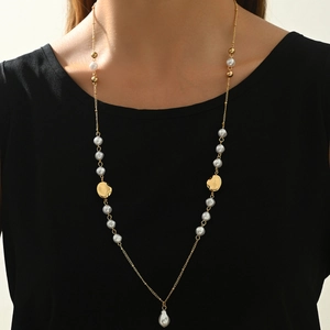 Detail of a 14K gold pearl necklace with irregular metal charms on a model's neck