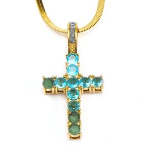 Macro shot of gold-tone cross pendant with blue and green crystals on snake chain