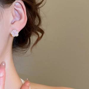 Close-up of pink flower earrings with golden edges and crystals on female ear