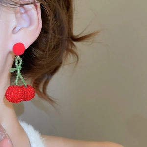 Macro detail of handmade red beaded cherry earrings with soft plush ball and green leaf