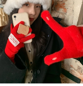 Close-up of red knit gloves with white lettered tag worn for a stylish mirror selfie