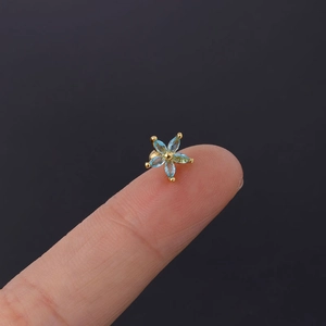 Macro shot of tiny blue zircon daisy earring on a fingertip for size scale reference