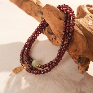 Red garnet beaded bracelet with green jade and gold Fu pendant on vintage wood background