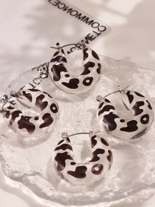 Macro shot of U-shaped resin hoop earrings with cow pattern on a glass tray