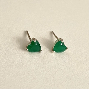 Macro detail of green heart-shaped emerald stones in silver prong-set stud earrings