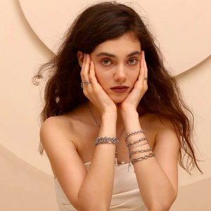 Close-up of layered silver chain bracelets and rings featuring paperclip links on a model