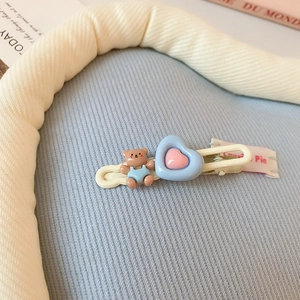 Détail de la pince à cheveux crème avec ours bleu et breloque de cœur rose pour fille