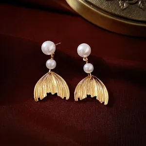 Macro detail of vintage pearl earrings with golden fish tail charms on textured fabric