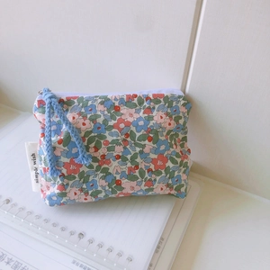 Floral mini cotton pouch with white zipper and blue pull cord on a notebook base