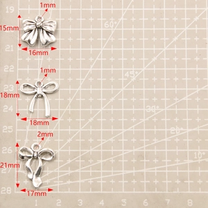 Three assorted silver bow alloy pendants with detailed size measurements on grid mat