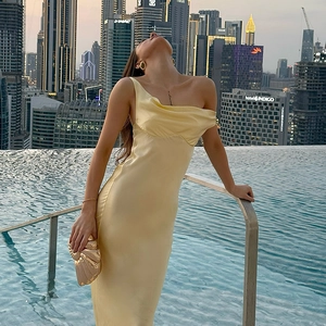 Détail d'une robe longue en satin jaune avec lustre soyeux et pochette coquillage dorée