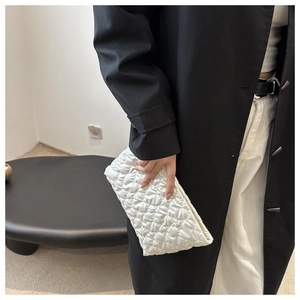 Detail showing a silver quilted clutch bag held by a model in a stylish black coat