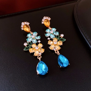 Detailed macro view of crystal flower earrings with blue teardrop pendants on black leather