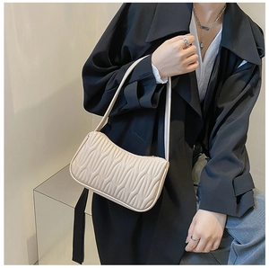 Detail of cream-colored shoulder bag with wave texture worn over a black blazer