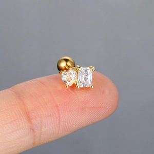 Macro shot of gold ear stud with heart and rectangle zircons held on a fingertip